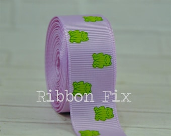 May include: A roll of lavender ribbon featuring a repeating pattern of green frog illustrations. The text "Ribbon Fix" is printed in white on the ribbon. This ribbon is suitable for crafts and gift wrapping.
