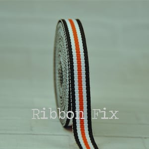 May include: Black, white, and orange striped ribbon. The ribbon is rolled up and the end is hanging down.