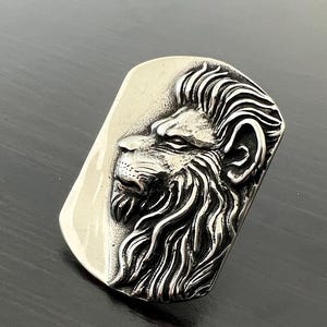 Pode incluir: Um pingente de prata com uma escultura tridimensional detalhada de uma cabe&ccedil;a de le&atilde;o. A juba do le&atilde;o &eacute; esculpida de forma intrincada e o pingente tem uma forma retangular.