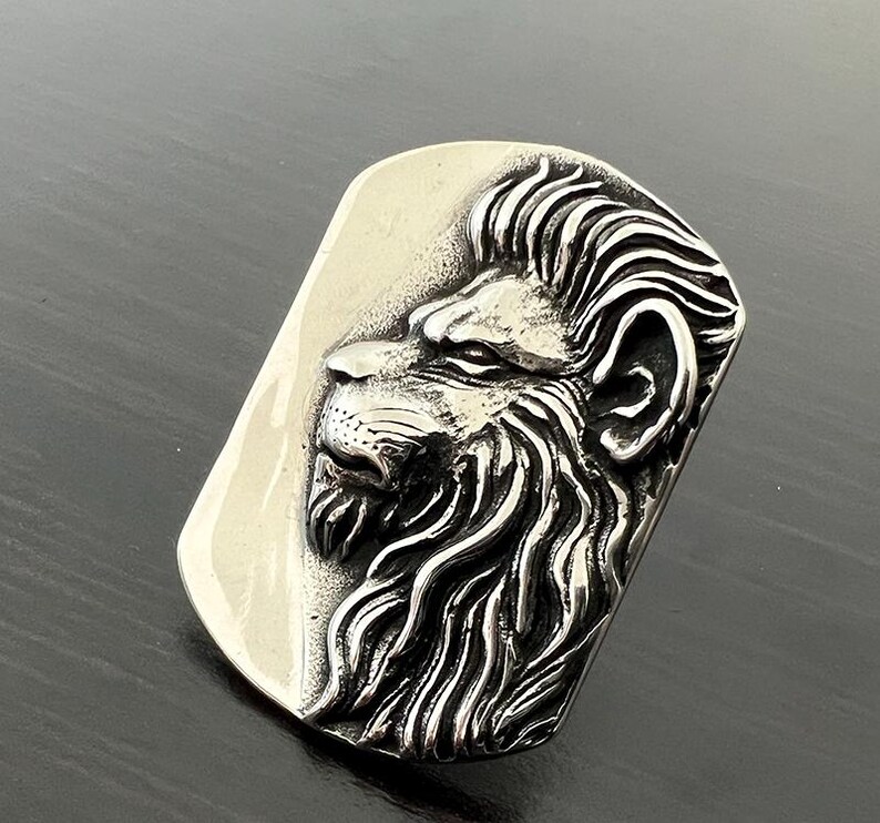 Pode incluir: Um pingente de prata com uma escultura tridimensional detalhada de uma cabe&ccedil;a de le&atilde;o. A juba do le&atilde;o &eacute; esculpida de forma intrincada e o pingente tem uma forma retangular.