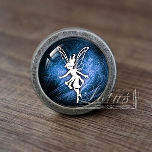 May include: A silver knob with a blue and white glass insert featuring a fairy silhouette. The fairy is white with wings and a flowing dress.