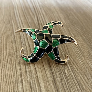 May include: A gold-tone brooch shaped like a starfish with black and green enamel. The starfish has a geometric pattern.