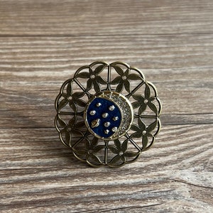 May include: A gold-toned metal ring with a delicate floral design. The centre of the ring features a blue crescent moon with white stars and a small planet.