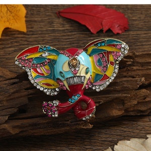 May include: A colourful enamel elephant brooch with rhinestones. The elephant is red, yellow, blue, green, and pink. The brooch is a whimsical and decorative piece of jewellery.