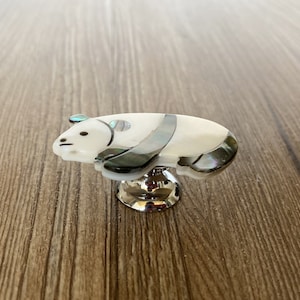 Puede incluir: Un pomo de armario en forma de panda blanco y negro con una base plateada. El panda est&aacute; hecho de n&aacute;car.