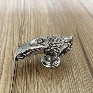 May include: Silver eagle head cabinet knob with a detailed design. The knob has a round base.