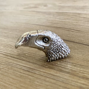 May include: A silver-coloured bird head sculpture with a detailed beak and feathers.