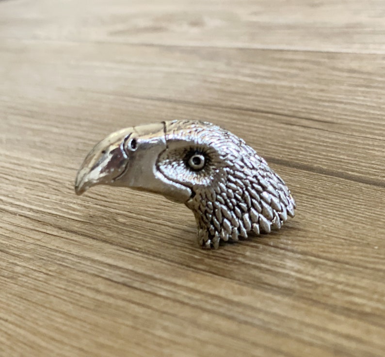 May include: A silver-coloured bird head sculpture with a detailed beak and feathers.