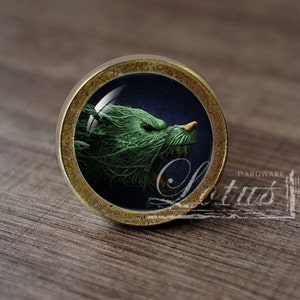 Può includere: Un pomello rotondo per armadio in ottone con un design di testa di lupo verde e ringhiante all'interno di una cupola di vetro.