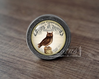 May include: A silver knob with a round, glass insert featuring an owl and the text "Societe Cooperative Pharmacies Populaires Liegeoises".