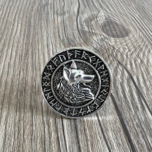 May include: A silver-toned metal pendant featuring a wolf's head surrounded by a circle of Norse runes.