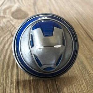May include: A silver belt buckle featuring a blue and silver Iron Man design.
