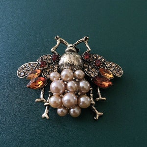 May include: A gold-toned bee brooch with a cluster of faux pearls in the center and orange and clear rhinestones on the wings.