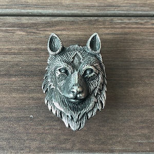 以下が含まれることがあります： 詳細なデザインが施された銀のオオカミの頭部の彫刻。彫刻は金属製で、リアルな外観をしています。