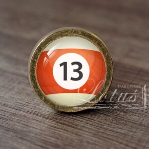 May include: A round, brass-colored knob with a glass insert featuring a red and white billiard ball with the number 13.