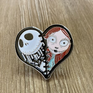 May include: A black and white heart-shaped enamel pin featuring Jack Skellington and Sally from the Nightmare Before Christmas movie. The pin is split in half, with Jack on the left and Sally on the right.