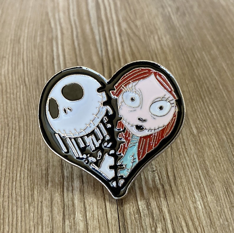 May include: A black and white heart-shaped enamel pin featuring Jack Skellington and Sally from the Nightmare Before Christmas movie. The pin is split in half, with Jack on the left and Sally on the right.