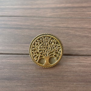May include: A gold-toned metal pendant featuring a detailed tree of life design. The pendant is circular and has a textured border.