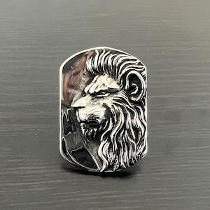May include: A silver ring with a detailed lion head design. The lion's head is facing to the side and has a textured mane.