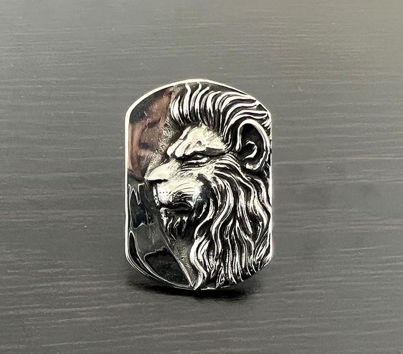 Pode incluir: Um anel de prata com um design detalhado de cabe&ccedil;a de le&atilde;o. A cabe&ccedil;a de le&atilde;o est&aacute; virada para o lado e tem uma juba texturizada.