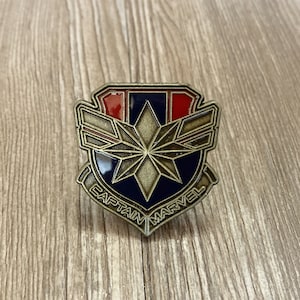 以下が含まれることがあります： 青、赤、白の星模様の銀色の金属製のピン。ピンには「キャプテン・マーベル」と書いてあります。