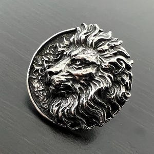 Peut inclure: Un pendentif en argent repr&eacute;sentant une t&ecirc;te de lion avec un design d&eacute;taill&eacute;. La crini&egrave;re du lion est flottante et les yeux sont intenses.