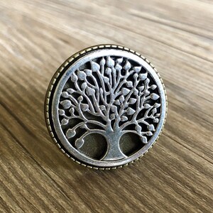 May include: A silver and gold tree of life pendant with a detailed design. The pendant is round and has a textured border.