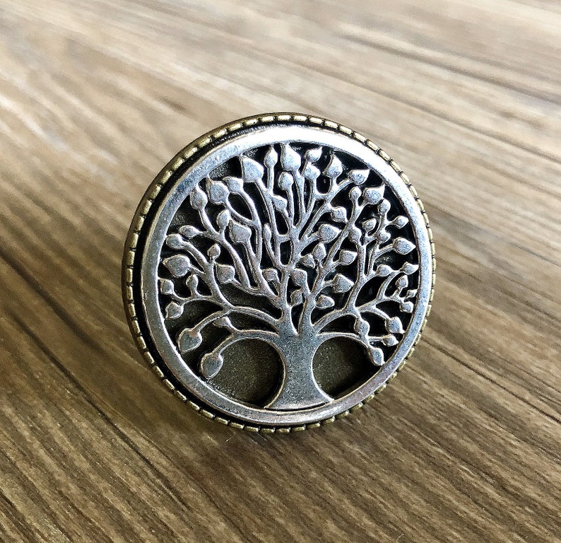May include: A silver and gold tree of life pendant with a detailed design. The pendant is round and has a textured border.