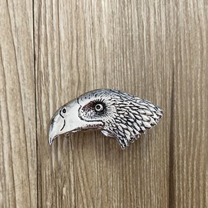 May include: A silver metal eagle head belt buckle with a detailed design.