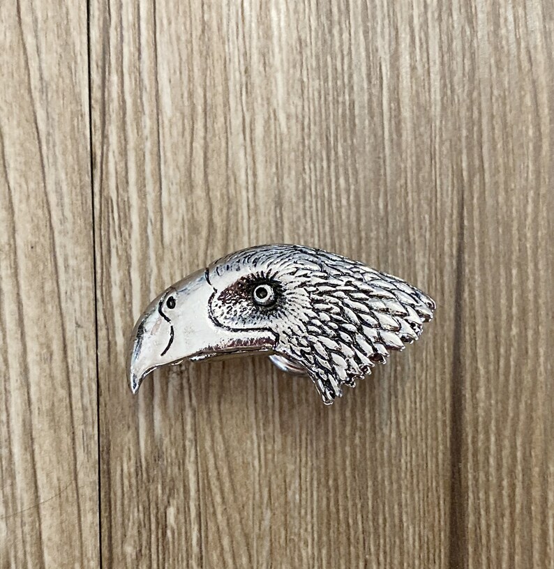 May include: A silver metal eagle head belt buckle with a detailed design.