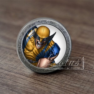 Könnte beinhalten: Ein runder, silberfarbener Schrankknopf mit weißem Hintergrund und einem bunten Bild von Wolverine, einem Comic-Superhelden, mit gelber und blauer Kleidung.