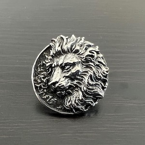 May include: A silver ring with a detailed lion head design. The lion's mane is intricately sculpted and the ring has a polished finish.