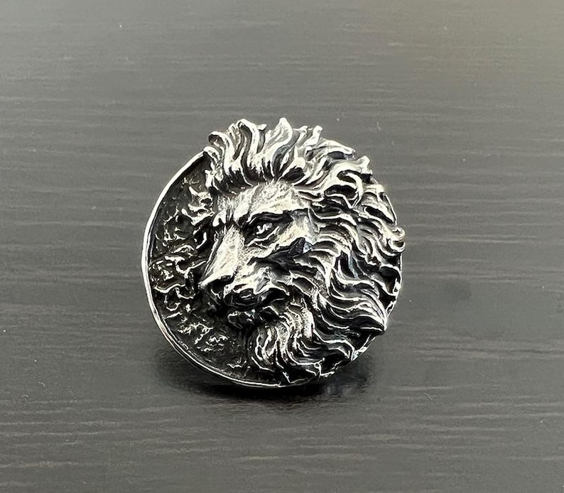 Peut inclure: Une bague en argent avec un motif de t&ecirc;te de lion d&eacute;taill&eacute;. La crini&egrave;re du lion est sculpt&eacute;e de mani&egrave;re complexe et la bague a une finition polie.