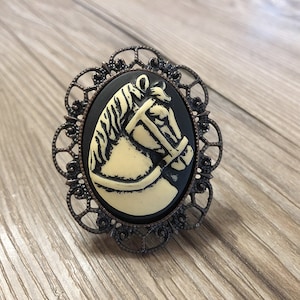 Peut inclure: Un camée noir avec un motif de tête de cheval blanc, serti dans un cadre en filigrane bronze.