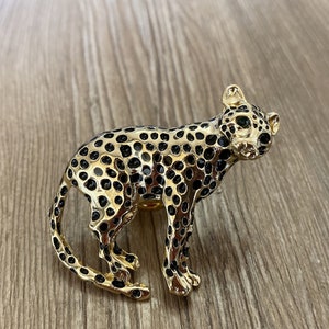 Peut inclure: Une broche en forme de l&eacute;opard dor&eacute;e avec des taches noires. Le l&eacute;opard a des yeux verts et un design d&eacute;taill&eacute;.