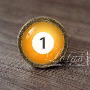 May include: A gold-toned cabinet knob with a round, orange glass insert featuring a white circle with the number "1" in black.