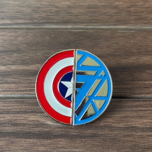 Può includere: Uno spillo di metallo circolare con un design diviso. Una metà presenta lo scudo di Captain America in rosso, bianco e blu. L'altra metà presenta il reattore ad arco di Iron Man in blu e argento.