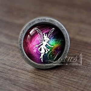 May include: A silver cabinet knob with a glass insert featuring a white fairy silhouette against a colorful galaxy background.