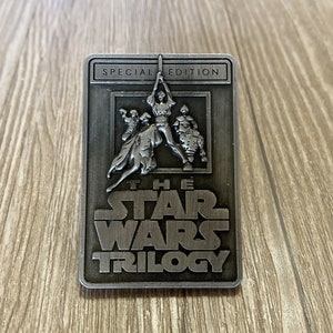 Op de afbeelding: Een rechthoekige, zilverkleurige metalen plaat met een reliëf van personages uit de Star Wars-trilogie. De bovenkant van de plaat leest "SPECIAL EDITION". Onder de afbeelding staat de tekst "THE STAR WARS TRILOGY".