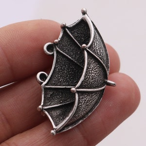 以下が含まれることがあります： 傘の形をした銀色の金属製のチャーム。傘は、質感のある表面に詳細なデザインが施されています。