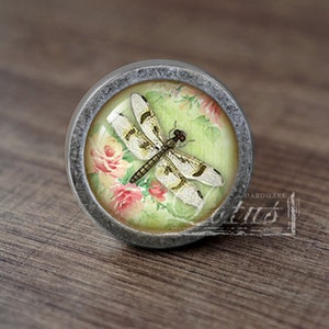 May include: A silver knob with a glass insert featuring a dragonfly and pink flowers on a green background.