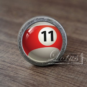 Op de afbeelding: Een zilverkleurige kastknop met een rood-wit biljartbalontwerp. De bal heeft het nummer "11" erop gedrukt.