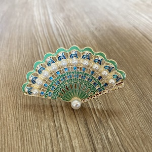 May include: A gold-tone fan-shaped brooch with green and blue enamel and faux pearl accents.