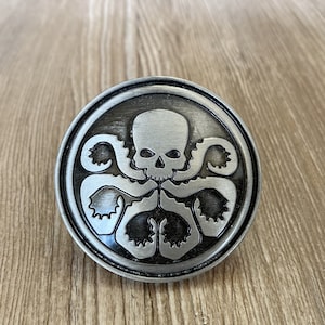 Könnte beinhalten: Eine silberfarbene Metallstifte mit einem schwarz-weißen Bild eines Schädels mit Tentakeln. Der Schädel hat einen bedrohlichen Ausdruck und die Tentakeln sind um ihn herumgewickelt.