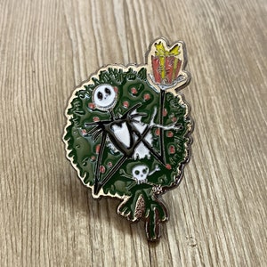 以下が含まれることがあります： ナイトメア・ビフォア・クリスマスのジャック・スケリントンがクリスマスツリーに扮した、黒と白のエナメルピン。赤いリボンと黄色のギフトボックスが乗っています。