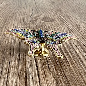 May include: A gold butterfly-shaped door knob with a colourful crystal design. The knob is mounted on a wooden surface.