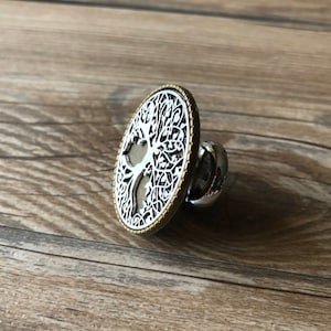 May include: A silver and gold metal ring with a tree of life design. The ring is round and has a detailed design of a tree with branches and leaves.