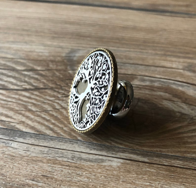 May include: A silver and gold metal ring with a tree of life design. The ring is round and has a detailed design of a tree with branches and leaves.