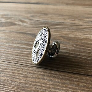 May include: A silver and gold round cabinet knob with a tree of life design.