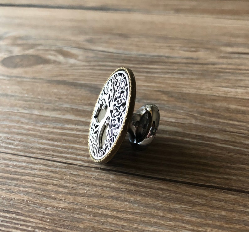 May include: A silver and gold round cabinet knob with a tree of life design.